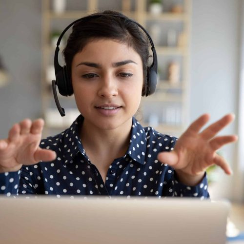 Indian woman teacher wear wireless headset video calling on laptop